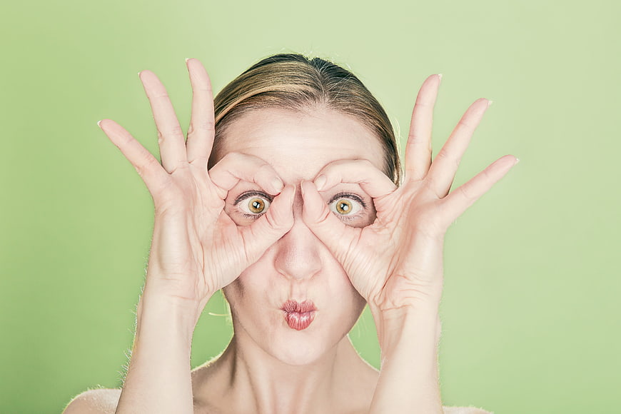 Playful young woman making funny face with hands on green background