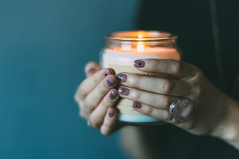 Woman holding lit candle with geometric nail art and ring
