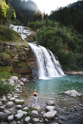 Woman standing by a cascading waterfall in a lush forest