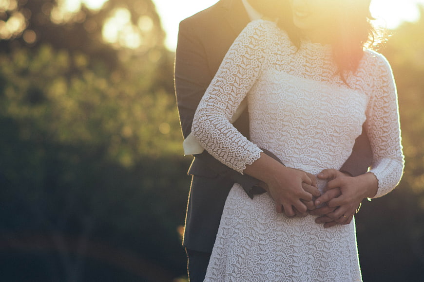 Romantic couple hugging in lace wedding dress at sunset