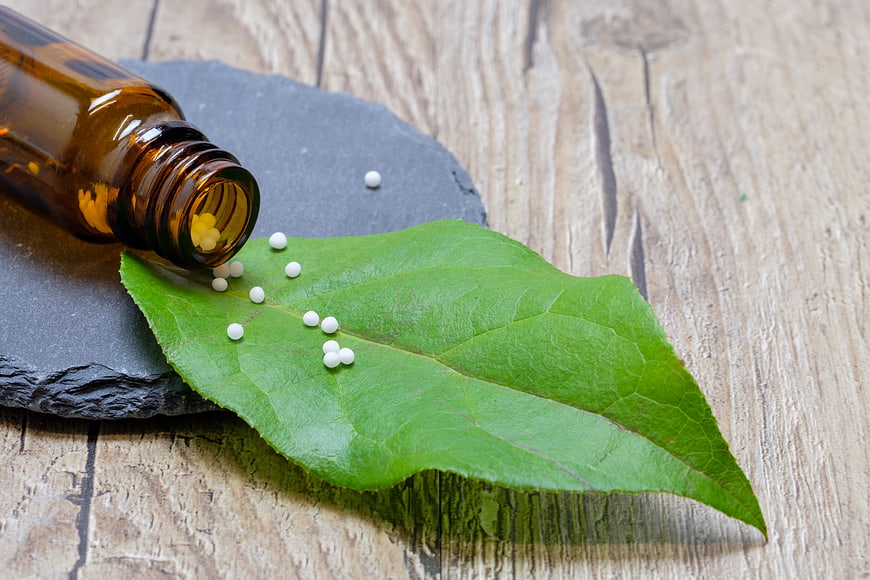Homeopathic globules spilling from amber bottle onto green leaf