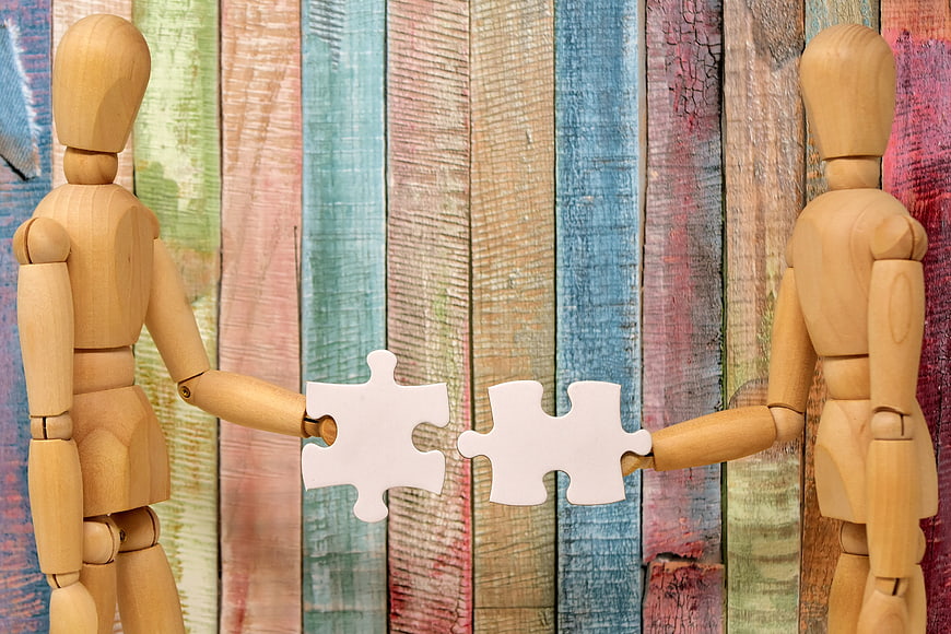 Two wooden mannequins holding puzzle pieces against colorful rustic background