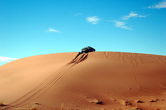 Off-road SUV driving over sand dune in desert