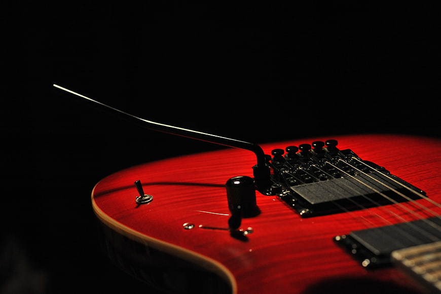 Close-up of red electric guitar body and bridge on black background