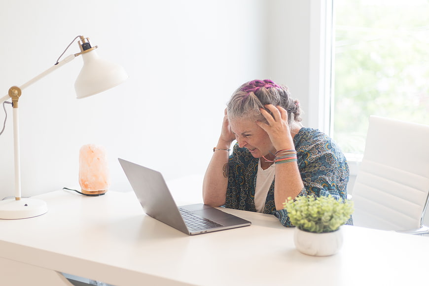 Frustrated Senior Woman with Pink Hair at Laptop