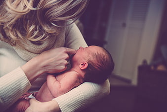 Mother holding newborn baby with finger in mouth