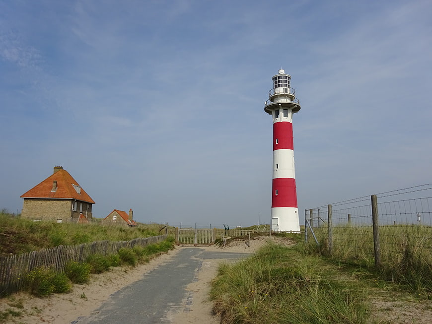Red and white lighthouse on sandy dunes with cottage