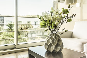 Modern ceramic vase with white flowers on a coffee table in a bright living room
