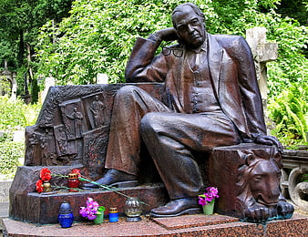Bronze statue of man sitting in cemetery with flowers