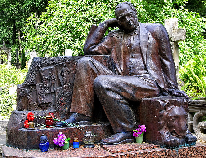Bronze statue of man sitting in cemetery with flowers