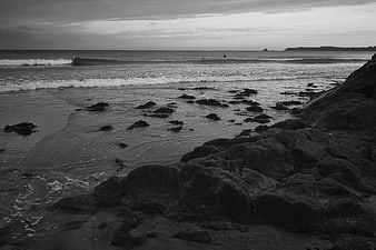Black and white rocky coastline with waves and surfers