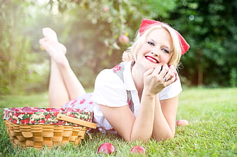Blonde woman lying on grass with basket of red apples