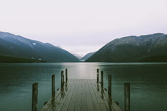 Serene wooden pier extending into calm lake with misty mountains