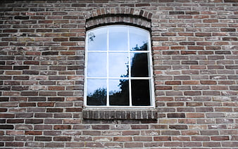 Arched window on old red brick wall with sky reflection
