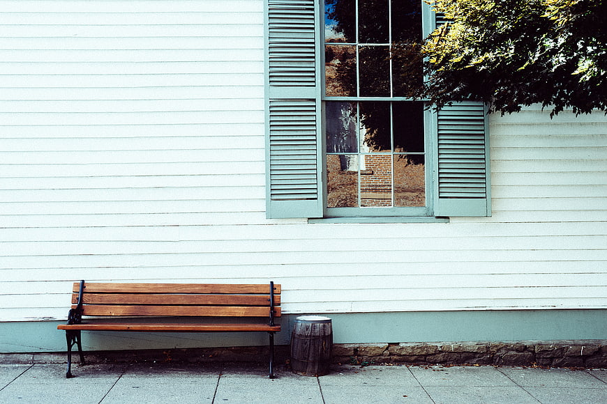 Empty wooden bench against white building with blue shutters