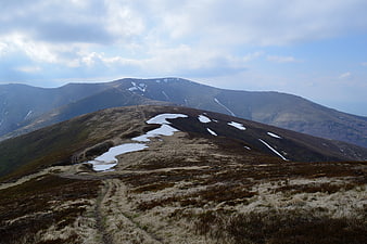 Mountain hiking trail with snow patches in spring landscape