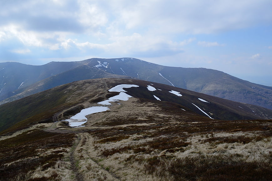 Mountain hiking trail with snow patches in spring landscape