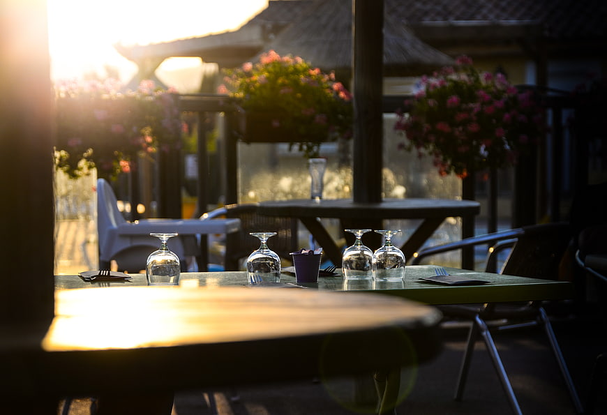Sunlit outdoor restaurant table with wine glasses and flowers