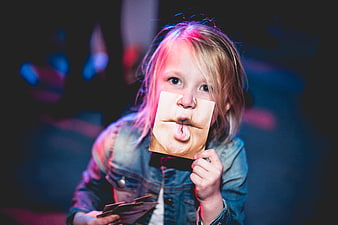 Child holding funny face cutout in neon light