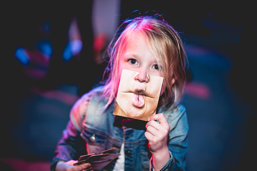 Child holding funny face cutout in neon light