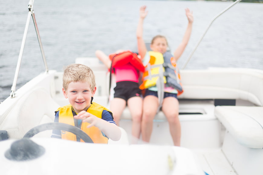 Happy Boy Steering Boat with Friends on Lake