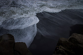 Aerial view of white ocean waves crashing on black sand beach