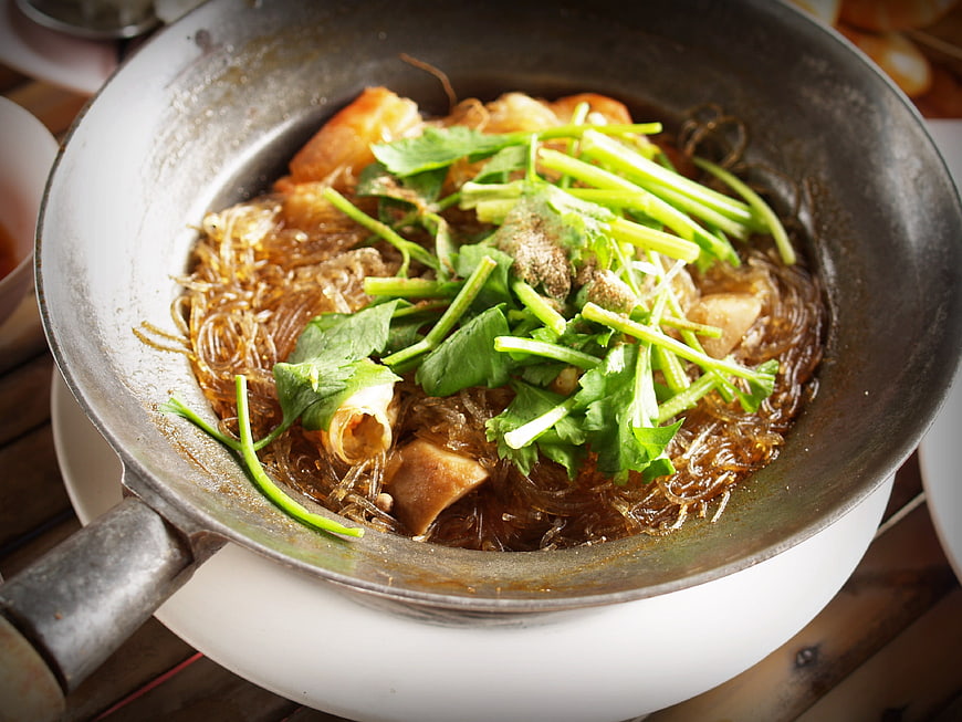 Steaming bowl of Asian noodles with fresh herbs and meat