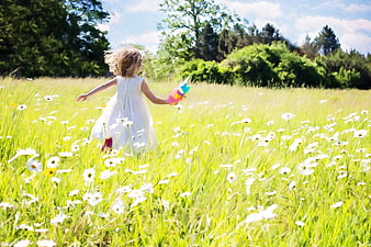Little girl running through daisy meadow with pinwheel