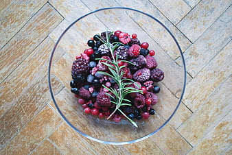 Top view of frozen mixed berries in a glass bowl on wood