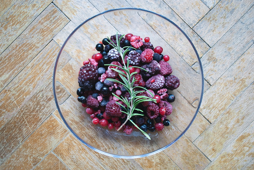 Top view of frozen mixed berries in a glass bowl on wood