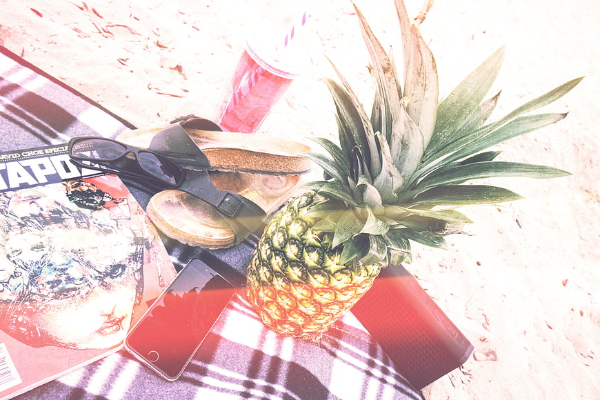 Summer beach picnic flat lay with pineapple, magazine, and sunglasses