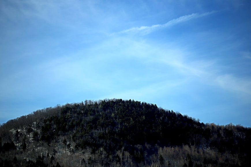 Silhouette of Forested Mountain Peak Against Blue Sky