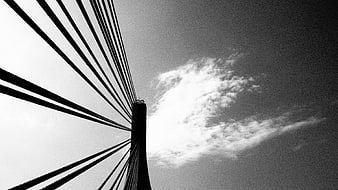 Black and white cable-stayed bridge tower against cloudy sky