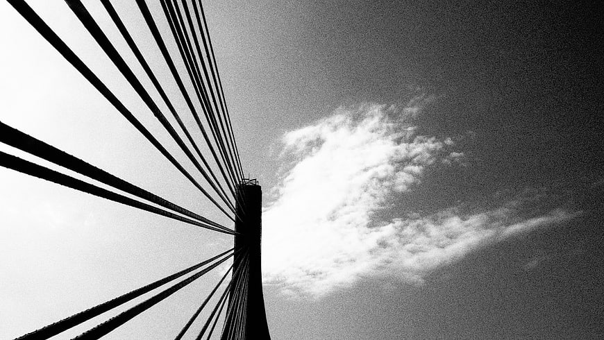 Black and white cable-stayed bridge tower against cloudy sky