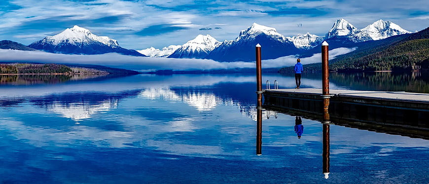 Person Standing on Dock with Snowy Mountain Reflection
