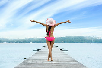 Woman in Pink Bikini on Wooden Pier with Arms Outstretched