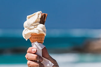 Hand holding melting vanilla ice cream cone on beach