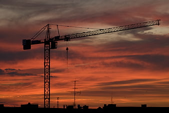 Silhouette of Construction Crane Against Dramatic Orange Sunset Sky