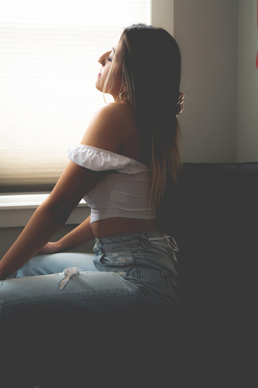 Young woman sitting by window in white top and jeans