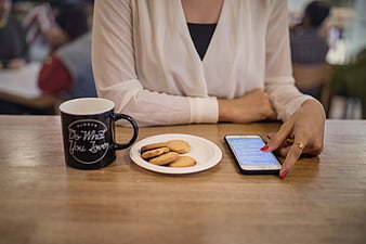 Woman using smartphone with coffee and cookies in cafe