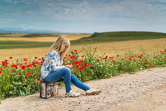 Woman sitting on suitcase by poppy field road