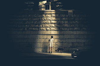 Woman Walking Dog at Night Against Stone Wall