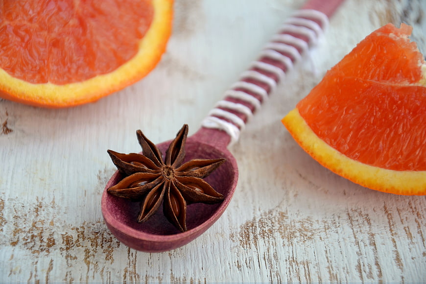 Star anise on wooden spoon with sliced blood orange