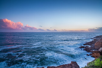 Dramatic Coastal Sunset with Pink Clouds and Crashing Waves