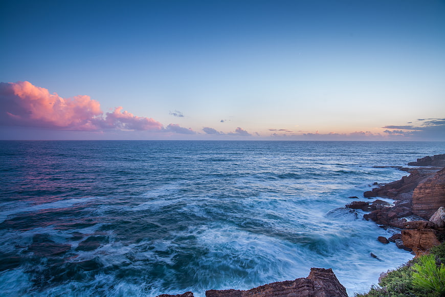 Dramatic Coastal Sunset with Pink Clouds and Crashing Waves