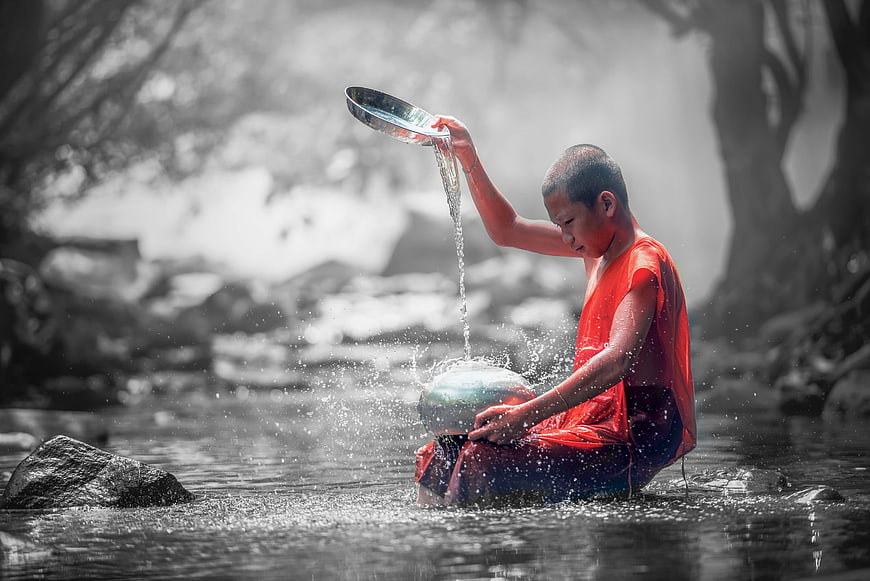 Young Buddhist monk performing water ritual in a forest stream