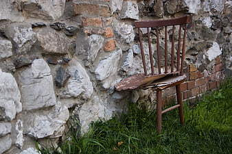 Broken wooden chair against old stone wall