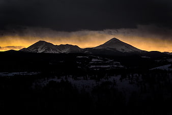 Dramatic sunset over snow-capped mountain peaks with dark foreground