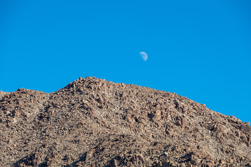 Rocky Desert Mountain Peak with Moon in Blue Sky