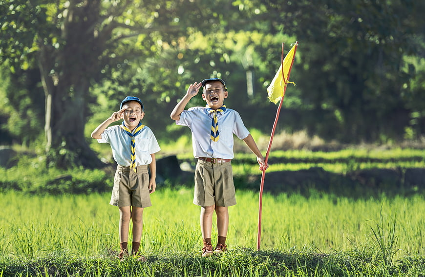 Two young Asian boy scouts saluting in a green field
